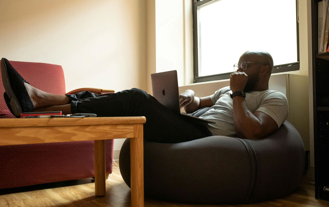 A guy on a bean bag chair with his feet up on the table browsing on his Macbook Pro.