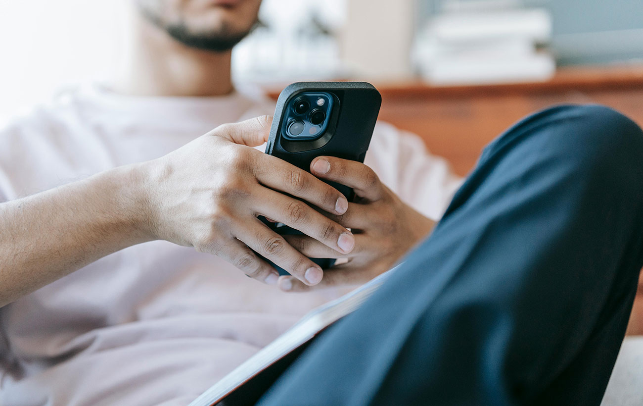 A guy in a white shirt and blue pants sitting down browsing on his phone